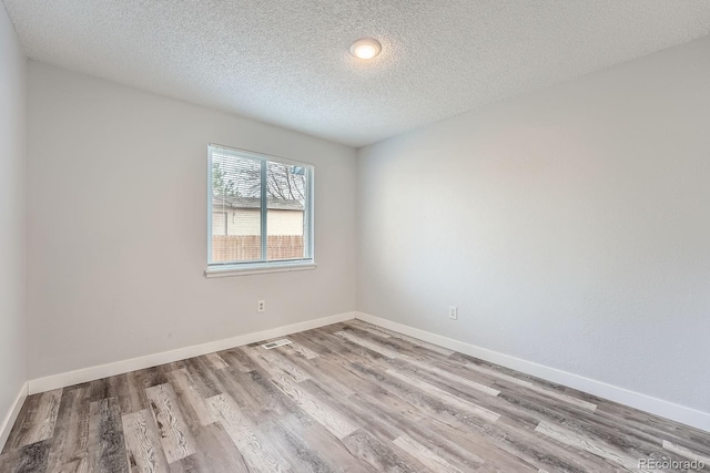 spare room featuring a textured ceiling, baseboards, and wood finished floors