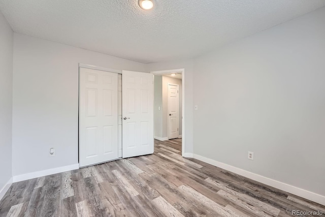 unfurnished bedroom with a textured ceiling, a closet, wood finished floors, and baseboards