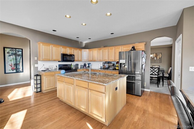 kitchen featuring an island with sink, light stone countertops, black appliances, light hardwood / wood-style floors, and light brown cabinets