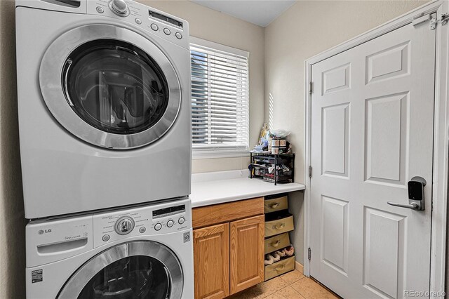 laundry room with light tile patterned flooring, cabinets, and stacked washer and clothes dryer