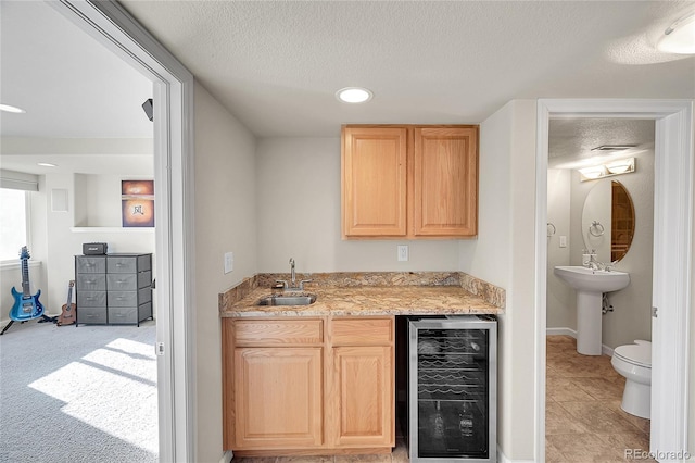 bar with sink, a textured ceiling, light brown cabinets, and wine cooler