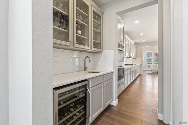 bar featuring backsplash, sink, dark hardwood / wood-style floors, stainless steel appliances, and beverage cooler