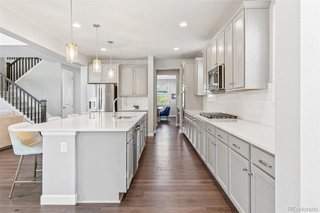 kitchen featuring appliances with stainless steel finishes, dark hardwood / wood-style flooring, sink, decorative light fixtures, and an island with sink