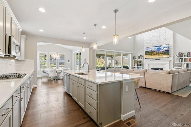 kitchen featuring sink, a stone fireplace, dark hardwood / wood-style floors, pendant lighting, and a kitchen island with sink