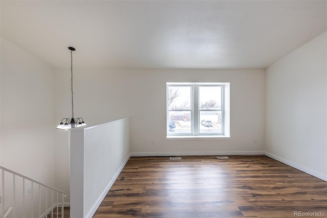 unfurnished room with a chandelier, baseboards, and wood finished floors