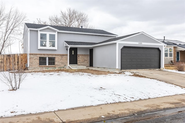 split level home featuring a garage, brick siding, fence, driveway, and roof with shingles