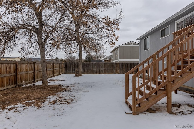 snowy yard with a fenced backyard and stairs