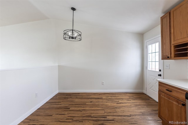 unfurnished dining area with dark wood-type flooring, lofted ceiling, baseboards, and an inviting chandelier