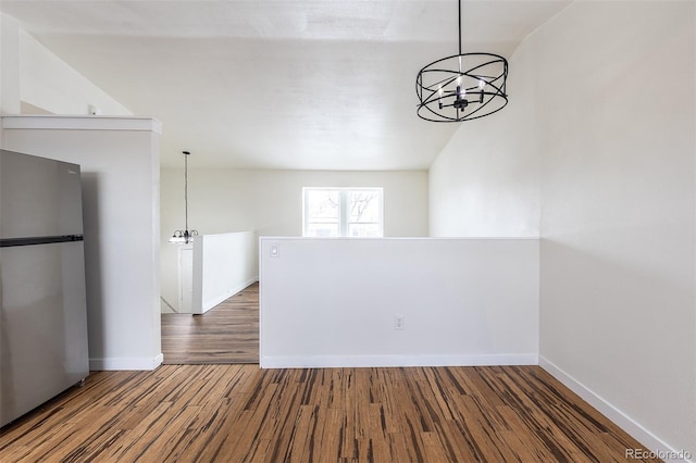 spare room with a chandelier, wood finished floors, and baseboards