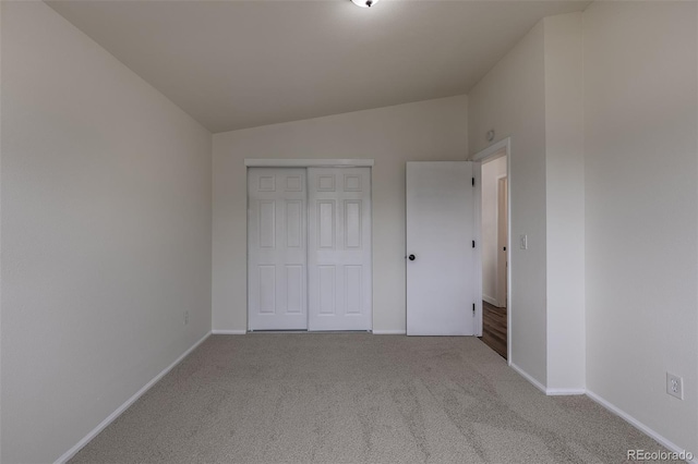 unfurnished bedroom with carpet, a closet, vaulted ceiling, and baseboards