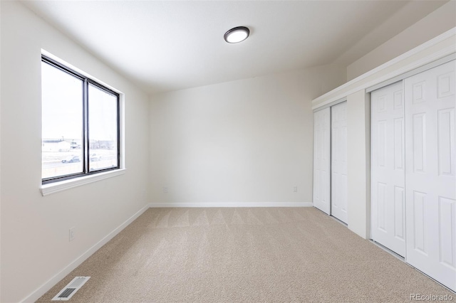 unfurnished bedroom featuring light carpet, baseboards, visible vents, and multiple closets