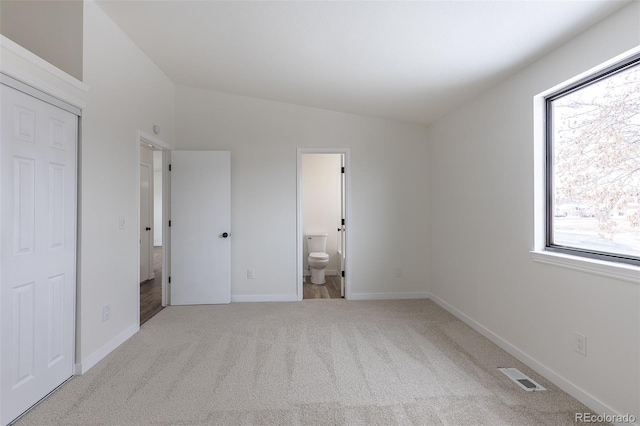 unfurnished bedroom featuring visible vents, baseboards, vaulted ceiling, carpet, and ensuite bath