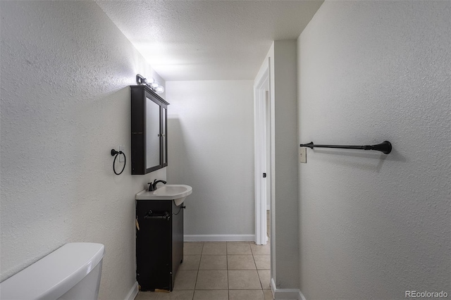 half bath featuring a textured ceiling, a textured wall, toilet, baseboards, and tile patterned floors