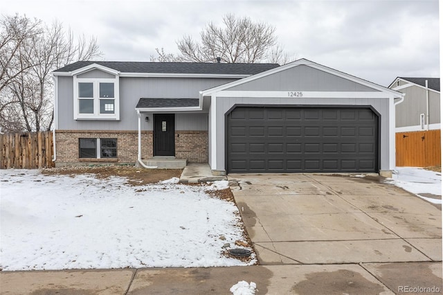 view of front of house with driveway, brick siding, an attached garage, and fence