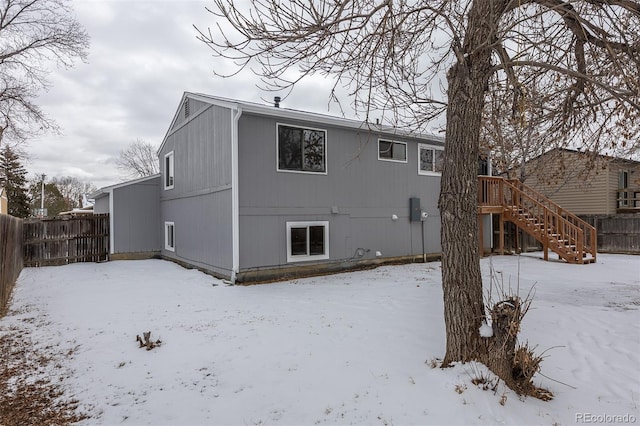 snow covered house featuring stairway and fence