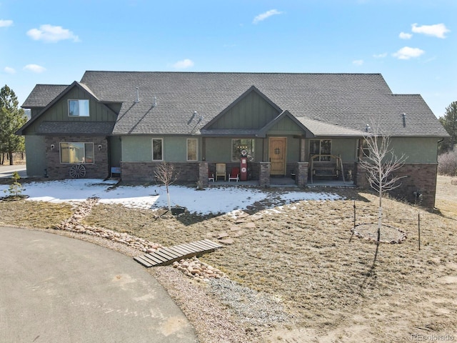 view of front facade with a porch, roof with shingles, board and batten siding, and brick siding