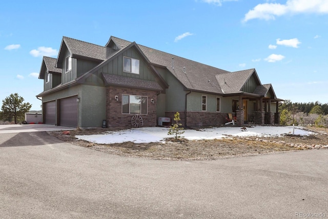 view of front of house featuring a garage, a shingled roof, brick siding, driveway, and board and batten siding