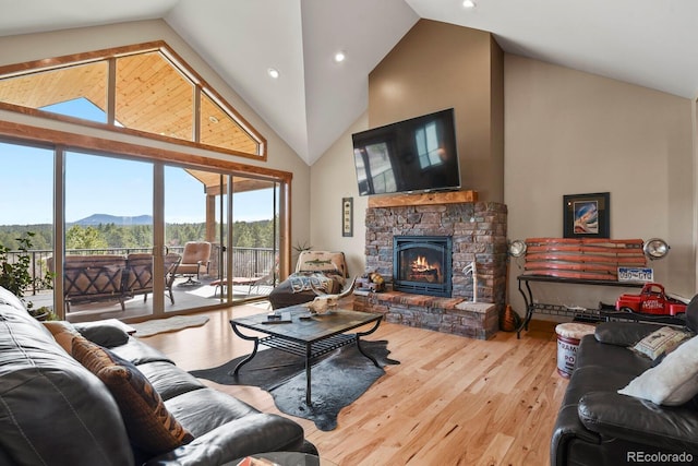 living area featuring high vaulted ceiling, a stone fireplace, wood finished floors, and recessed lighting