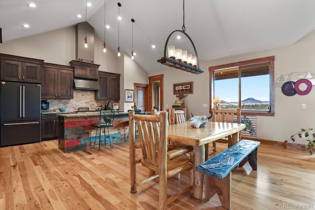 dining space with high vaulted ceiling and light wood-style floors