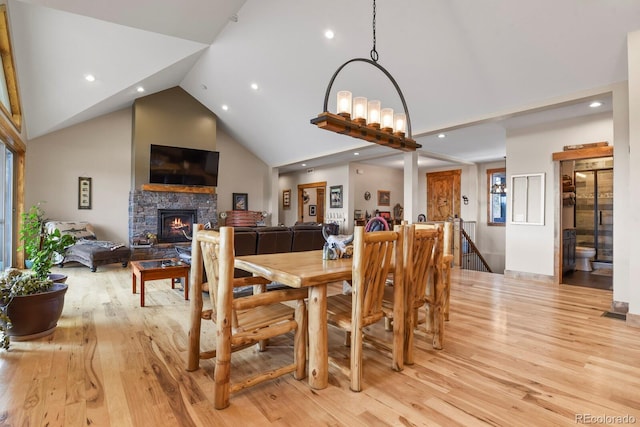 dining area with high vaulted ceiling, a stone fireplace, recessed lighting, and light wood-style floors