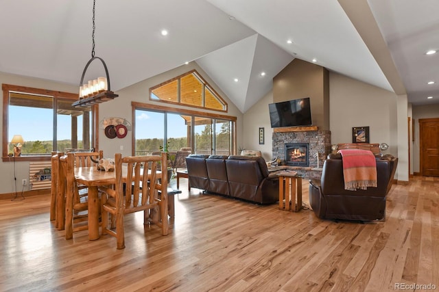 dining area with high vaulted ceiling, a wealth of natural light, a stone fireplace, and light wood finished floors