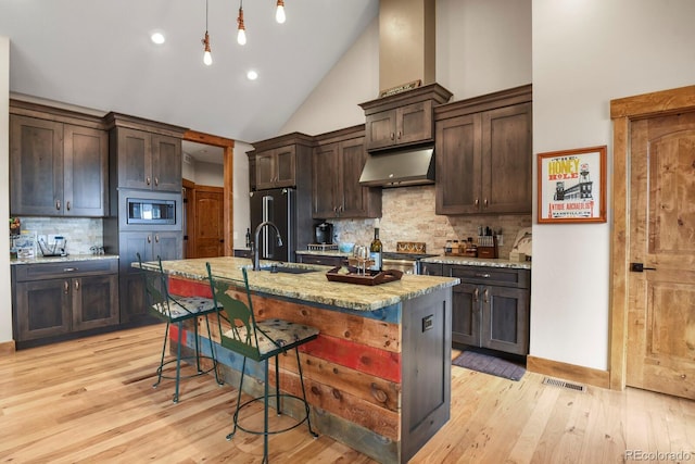 kitchen with under cabinet range hood, a sink, light wood-style floors, dark brown cabinets, and stainless steel microwave