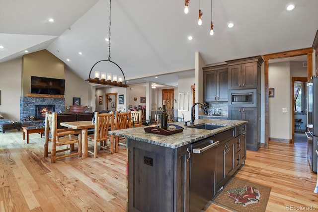 kitchen with dark brown cabinetry, open floor plan, stainless steel appliances, a stone fireplace, and a sink