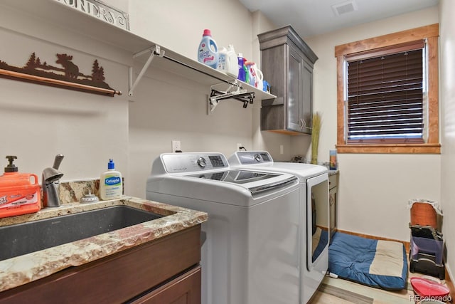 washroom with cabinet space, a sink, visible vents, and separate washer and dryer