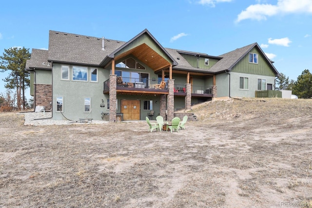 back of property featuring stone siding, roof with shingles, and a balcony