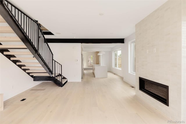 unfurnished living room featuring stairs, a tiled fireplace, and light wood finished floors