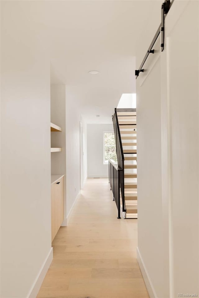 hallway featuring a barn door, baseboards, and light wood finished floors