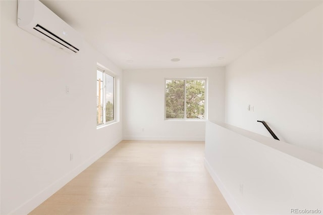 unfurnished room featuring a healthy amount of sunlight, baseboards, light wood-type flooring, and a wall unit AC