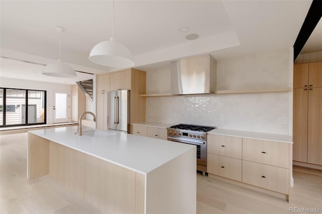 kitchen with a kitchen island with sink, high quality appliances, tasteful backsplash, hanging light fixtures, and wall chimney range hood