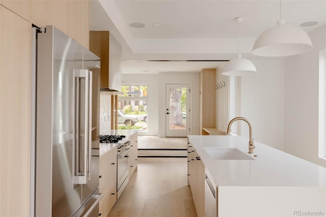 kitchen featuring decorative light fixtures, light hardwood / wood-style floors, sink, a center island with sink, and high quality appliances