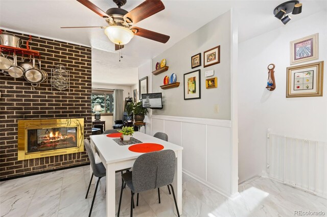9598 Lowell Blvd, Westminster, CO 80031 - dining area with marble look tile flooring, a fireplace, a ceiling fan, wainscoting, and a decorative wall