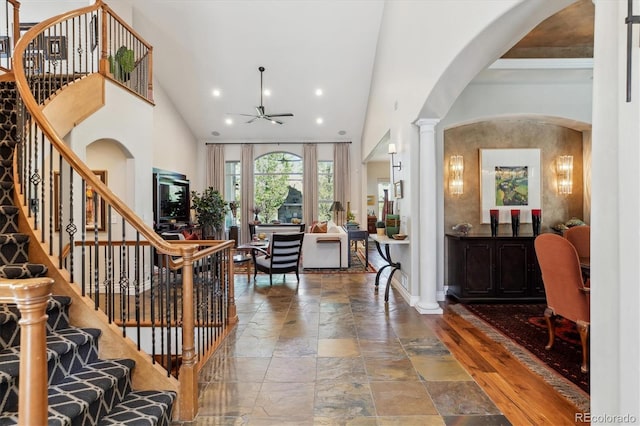 entrance foyer featuring stone tile flooring, a ceiling fan, arched walkways, and high vaulted ceiling