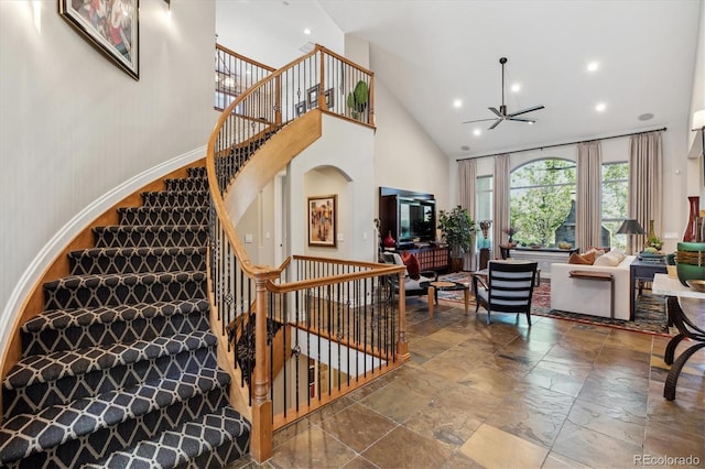 staircase with arched walkways, high vaulted ceiling, stone tile floors, a ceiling fan, and recessed lighting