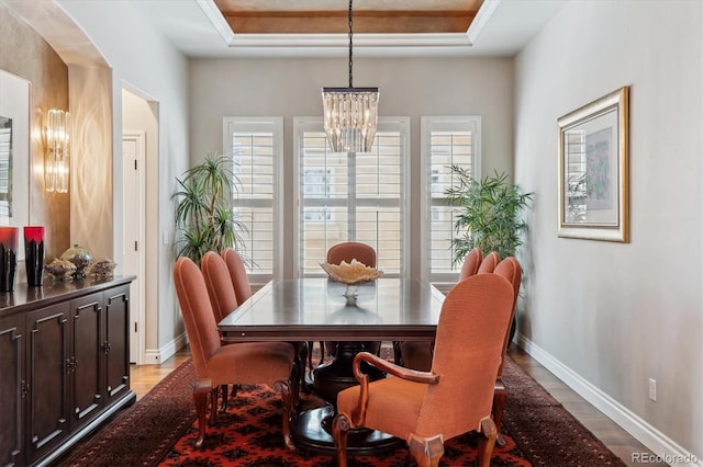 dining area with light wood-style floors, arched walkways, baseboards, an inviting chandelier, and a tray ceiling
