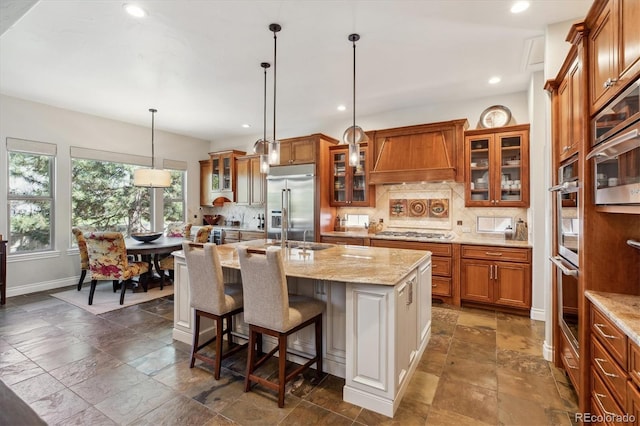 kitchen with appliances with stainless steel finishes, backsplash, brown cabinets, and stone tile flooring