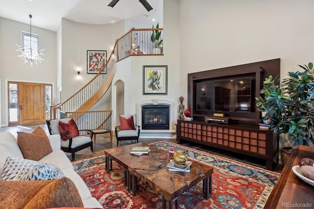 living area with an inviting chandelier, stairs, a glass covered fireplace, and a high ceiling