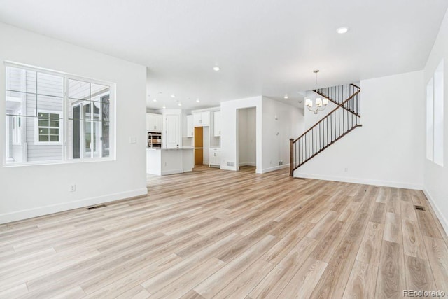 unfurnished living room with light hardwood / wood-style floors and a chandelier