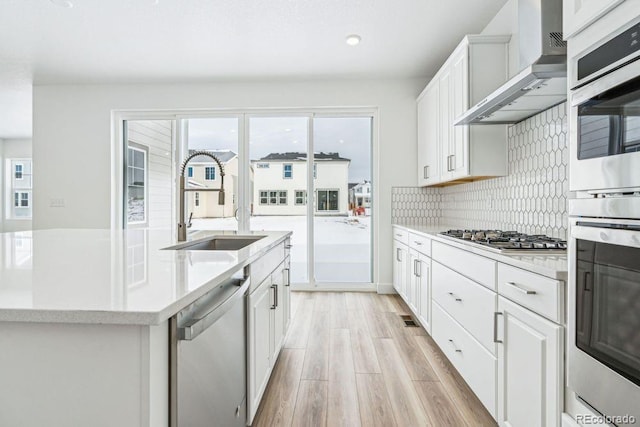 kitchen with stainless steel appliances, a center island with sink, white cabinets, and wall chimney exhaust hood