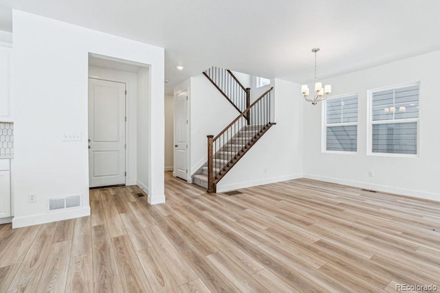 unfurnished room featuring a notable chandelier and light hardwood / wood-style flooring