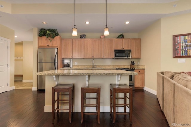 kitchen with appliances with stainless steel finishes, dark wood-type flooring, a breakfast bar area, and baseboards