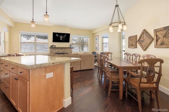 kitchen with a breakfast bar area, open floor plan, hanging light fixtures, light stone countertops, and dark wood finished floors