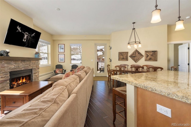 living area featuring a baseboard heating unit, dark wood-style flooring, and a stone fireplace