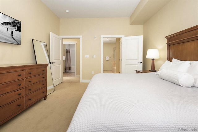 bedroom featuring light carpet, ensuite bathroom, a walk in closet, and baseboards