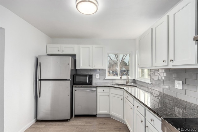 kitchen with sink, stainless steel appliances, light hardwood / wood-style floors, white cabinets, and dark stone counters