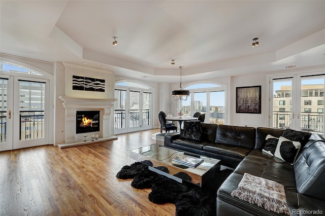 living area with a view of city, french doors, a raised ceiling, a glass covered fireplace, and wood finished floors