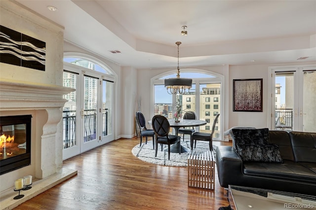 dining room with visible vents, a raised ceiling, wood finished floors, french doors, and a fireplace